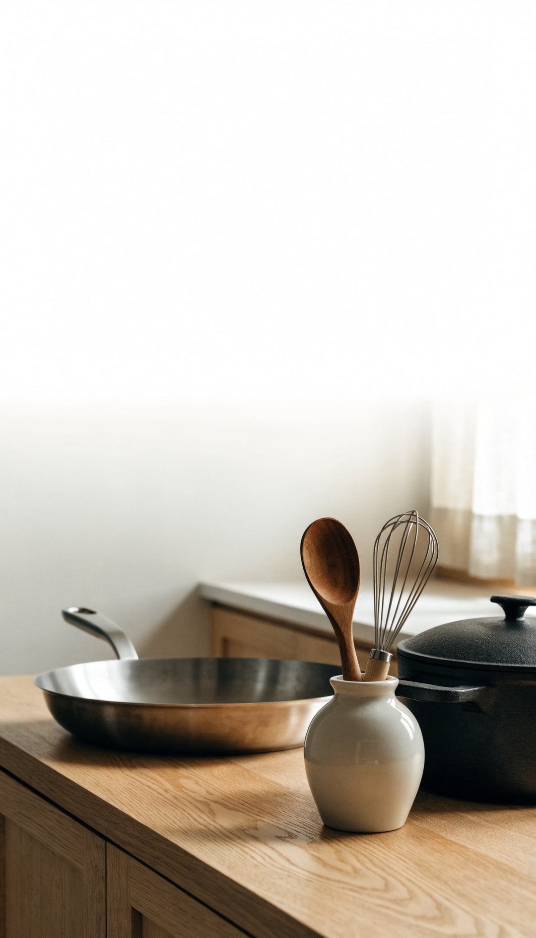 Poêle en inox et cocotte en fonte sur un plan de travail en chêne, lumière du jour