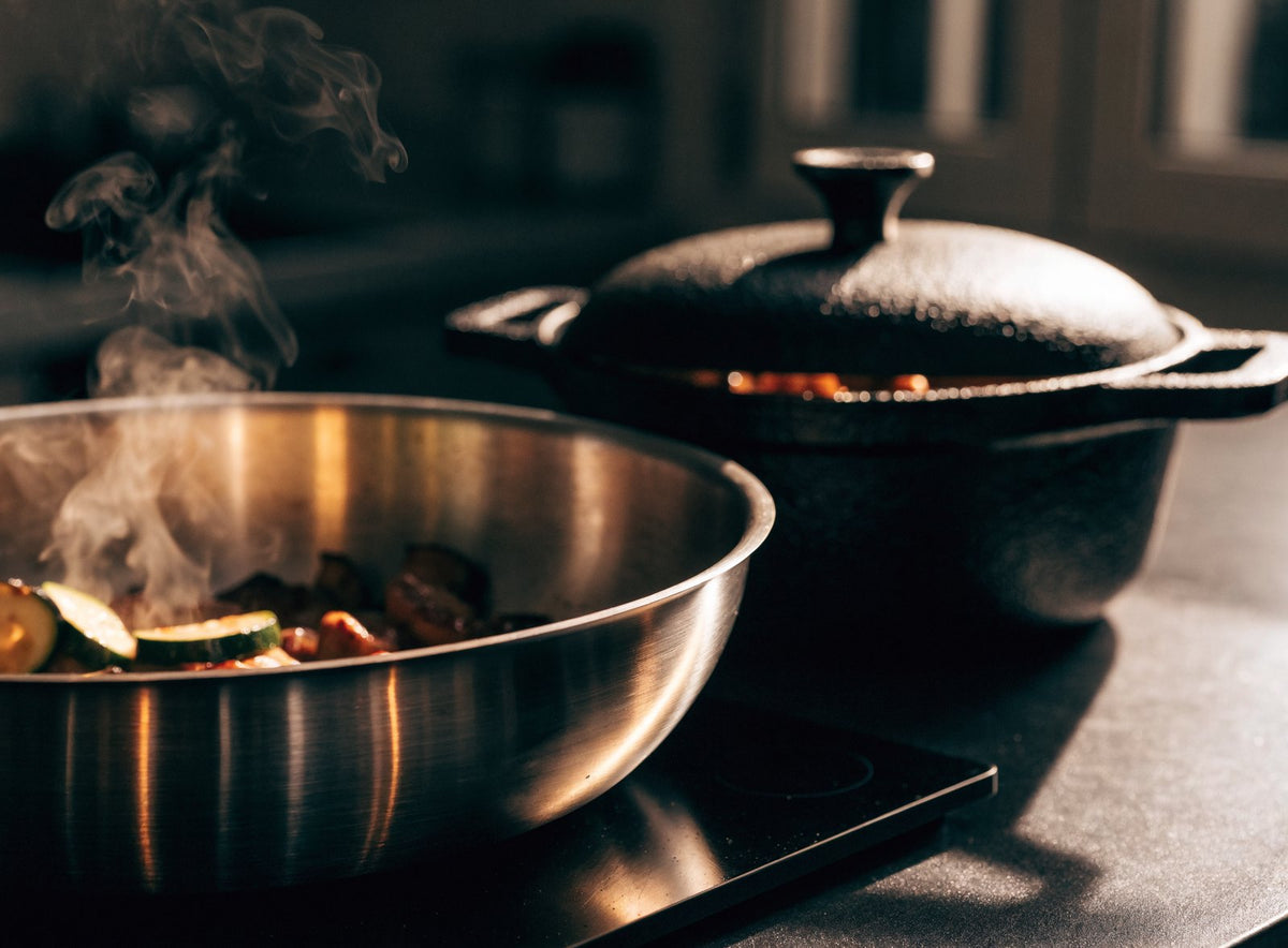 Poêle en inox qui saisit des légumes sur une plaque à induction, cocotte en fonte à côté Image